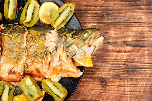 Roasted fish is served with kiwi slices and orange. Seafood dinner, fried trout, healthy dish.