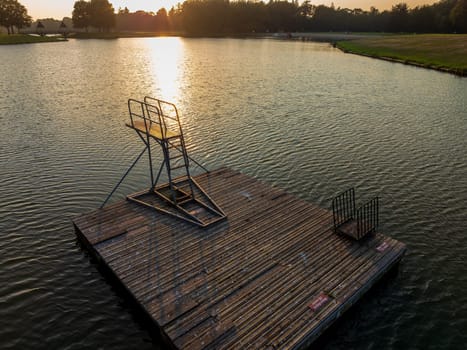 wooden floating platform with diving tower on a swimming lake at sunset
