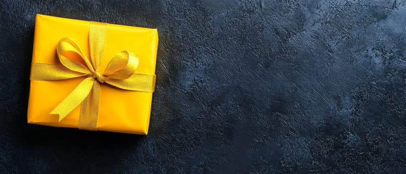 A vibrant yellow gift box with a bow sits on a dark textured background, ideal for celebrations and copy space.
