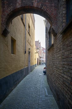 Woman sitting on a step in a narrow alley in Bruges, Belgium, talking on the phone