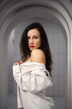 Brunette woman wearing a white off-the-shoulder shirt standing in profile in a corridor with a curved ceiling