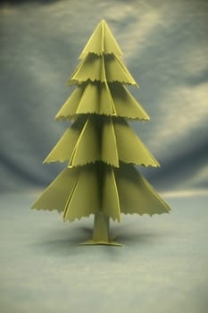 A vibrant green paper Christmas tree stands upright on a blue surface, showcasing a creative holiday decoration idea for festivities.
