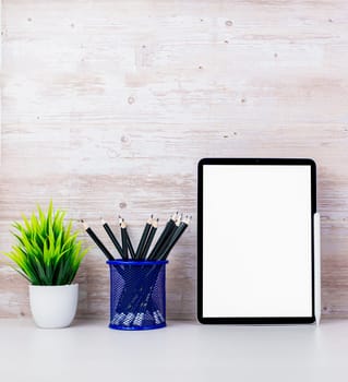 Tablet with blank screen placed on white table and leaning against wooden surface wall with office equipment. Copy space for your text. Workspace and copy space. Office desk with office supplies