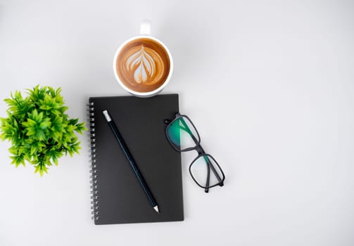 Top view white workspace office desk with office supplies. Flat lay work table with black notebook, Green leaf and coffee cup, Copy space for your advertising content.