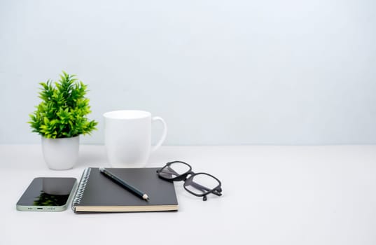 Workspace mock up white table top with vintage notebook, Pencils and green houseplant. Copy space desk with copy space for products display montage. Minimalist white workplace with supplies.