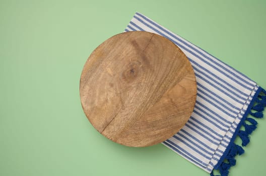 Empty round brown wooden cutting board on a greenk background, top view