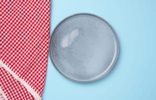 Round ceramic empty blue plate and red kitchen towel, top view