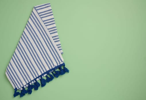 Folded linen striped kitchen towel on green background, top view