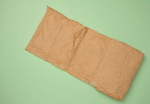 Roll of brown wrapping paper on green background, top view