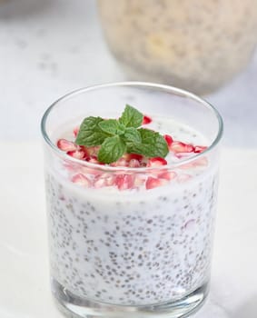 Glass with chia and yogurt dessert decorated with fresh fruits and pomegranate seeds on white table