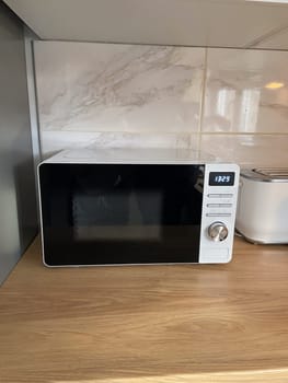 Modern kitchen corner features a microwave, a toaster on a wood countertop. Minimalist design with sleek white cabinets and marble backsplash creates a clean and organized cooking space
