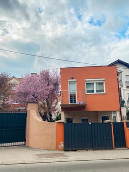 Residential building stands under a bright blue sky, with blossoming trees adding a touch of springtime charm to the scene. Peaceful atmosphere is enhanced by the natural beauty surrounding the architecture.