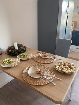 Festive dining table set with an assortment of homemade dishes, complemented by a decorative holiday wreath centerpiece. Warmth and joy of gathering for a shared meal during holiday season.