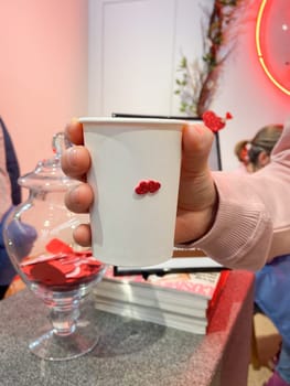 Close-up hand holds a cup of vibrant green matcha in a cozy cafe setting, Freshness of beverage. On background reveals a glimpse of the barista's workspace, filled with colorful straws and utensils