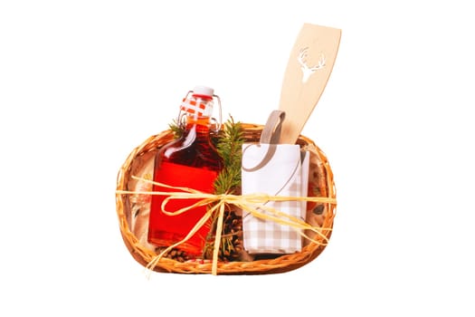 Closeup of a gift basket with swing top bottle with red alcohol, a folded shopping bag and a wooden spoon with punched out deer antler motif isolated. Top view.