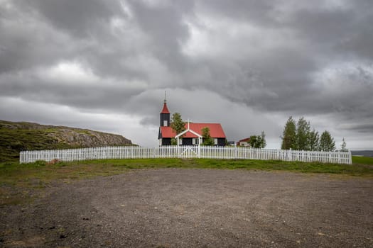 Small black and red church  behind a white fence Iceland