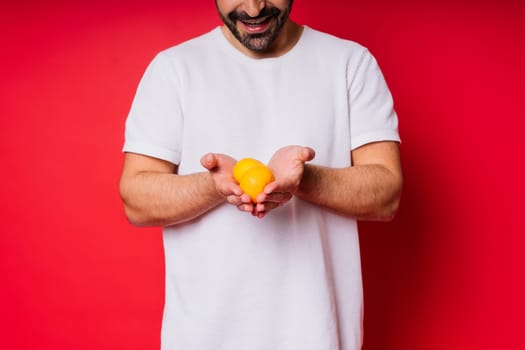 Handsome tall bearded white man with a dark hair with tangerine on red background