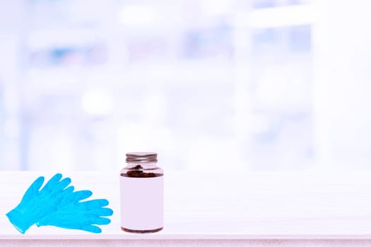 Closeup of a pair of blue medical doctor gloves or surgical gloves and a glass bottle medicine with empty label on table over abstract blurred hospital background. Space.