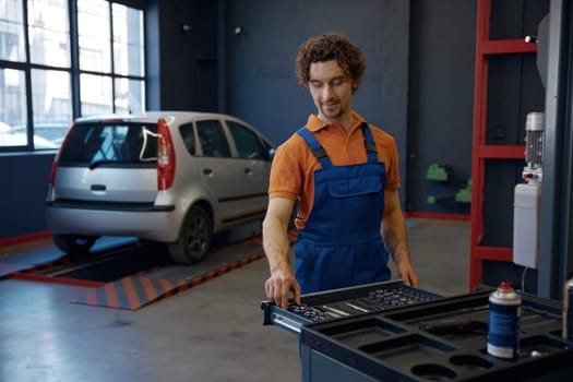 Man mechanic working at car repair service workshop. Male technician pushing trolley cat with tools and supplies for auto maintenance and tuning