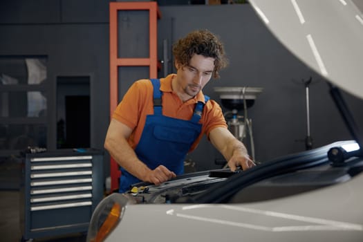 Male mechanic looking under car hood checking engine operation work. Auto diagnostic and repair service concept