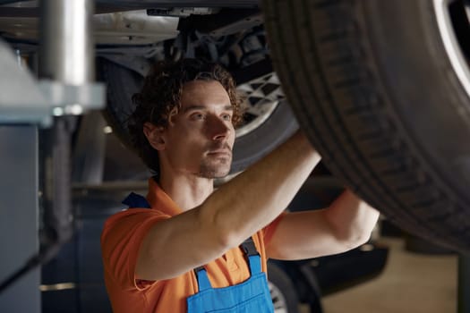 Professional mechanic repairing wheel fixing problem standing under car. Auto repairman checking springs and shocks in garage