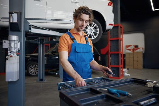 Tool box and male mechanic hands taking wrench for work. Professional repairman service at auto garage
