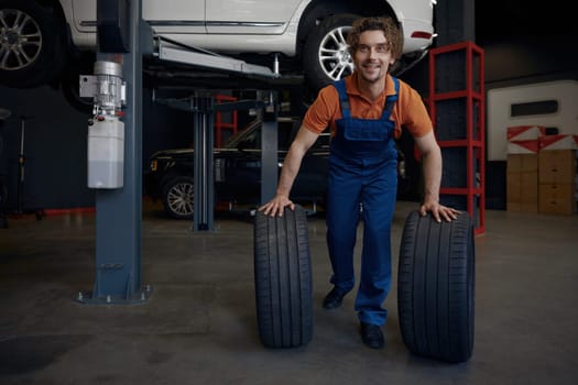 Repairman rolling car spare tires while working on wheel replacement providing professional automotive mechanical