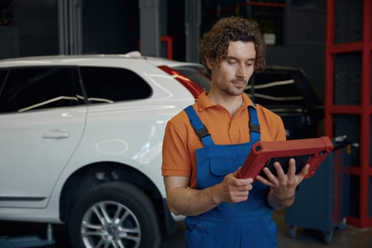 Portrait of serious male car technician looking at computer tablet while working with auto breakage at repair service station