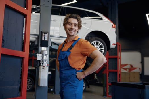 Professional male auto mechanic in uniform smiling with confidence posing for camera at car repair workshop