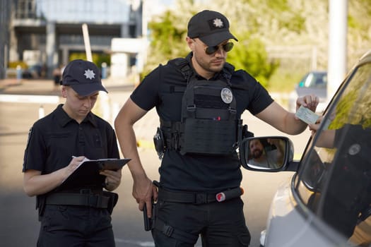 Patrolman and patrolwoman writing traffic ticket for parking violation. Street safety surveillance team at work