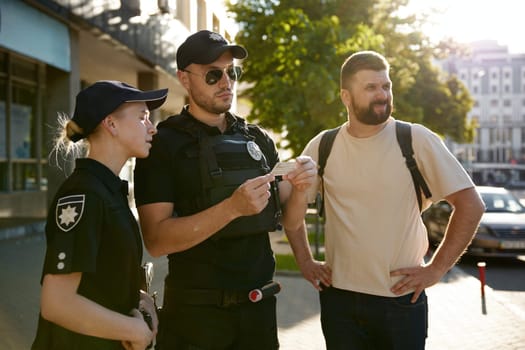 Serious patrol policeman and policewoman checking personal documents of citizen on city street