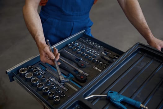 Closeup high angle view on tool box and male mechanic hands taking wrench for work cropped shot. Professional repairman service at auto garage