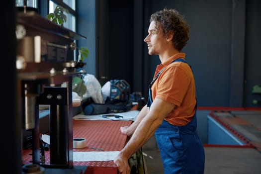 Male auto mechanic dreaming looking through window enjoying work break rest at garage shop