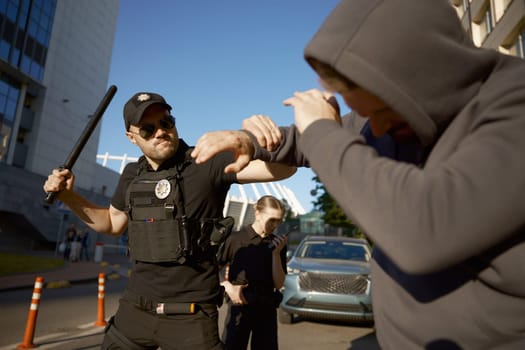Policeman with baton attacking aggressive male offender to arrest. Policewoman talking to radio reporting to police department