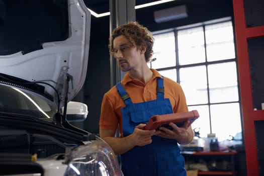Portrait of serious male car technician looking at computer tablet while working with auto breakage at repair service station