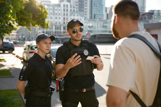 Patrol policeman and policewoman checking personal documents of citizen on city street