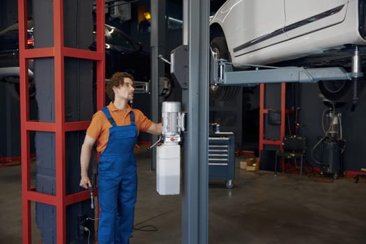 Male auto service worker lifting car for diagnostic and inspection on elevator at modern repair shop