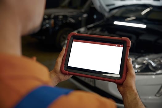 Over shoulder view on empty blank screen of tablet in auto mechanic hands. Scanning and diagnostics of damaged car electronic or engine at automotive repair workshop