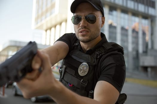 Portrait of concentrated man patrol police officer aiming with handgun in action standing outdoors in city street