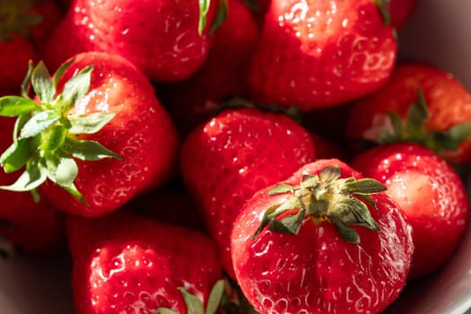 A bowl of red strawberries with green leaves. The strawberries are ripe and ready to eat. The bowl is white and the strawberries are the main focus of the image