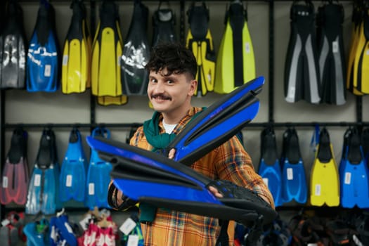 Funny hipster man holding flippers posing for camera over sportive shop showcase background. Shopping for scuba diving hobby concept