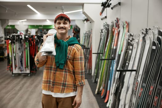 Portrait of happy satisfied man buying trendy ski gear posing for camera over sports shop background. Sporting goods purchase and touristic consumerism