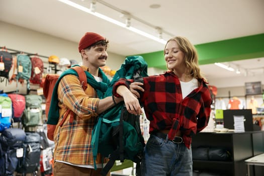 Happy young family couple of travelers shopping at sports store choosing backpack for personal belongings. Preparation for weekend cycling tour or camping outdoor picnic