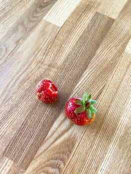 Two fresh strawberries on wooden table.