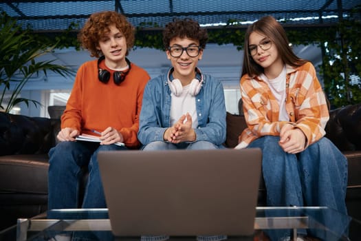 Team of teenagers having a work video call. Teens using laptop and headphones working online in office. Three young employees discussing new work project