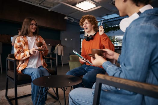 Excited teenagers talking at workplace. Two boys and girl relaxing after hard work day. Group of young workers enjoying conversation