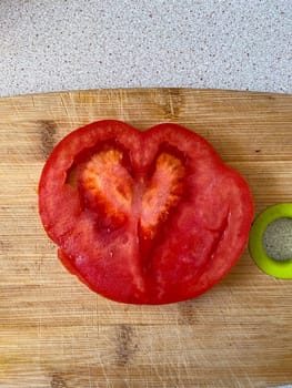 Vibrant tomato slice reveals a heart shaped pattern, resting on a wooden cutting board. Freshness of tomato adds a touch of nature artistry to a simple kitchen moment. Valentine day.