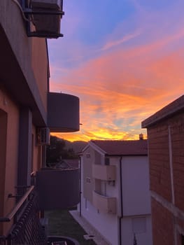 Vibrant sunset casts warm hues over residential buildings, creating a stunning contrast against evening sky. Peaceful transition from day to night, highlighting the serene beauty of urban life.