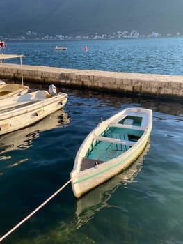Small wooden boat floats calmly in a serene harbor, tied to dock as gentle waves reflect surrounding landscape. Coastal life and tranquil maritime environments.