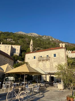 Outdoor cafe in a historic stone building nestled at base of green mountain under a clear blue sky. Tranquil blend of architecture and nature, perfect for a relaxed afternoon